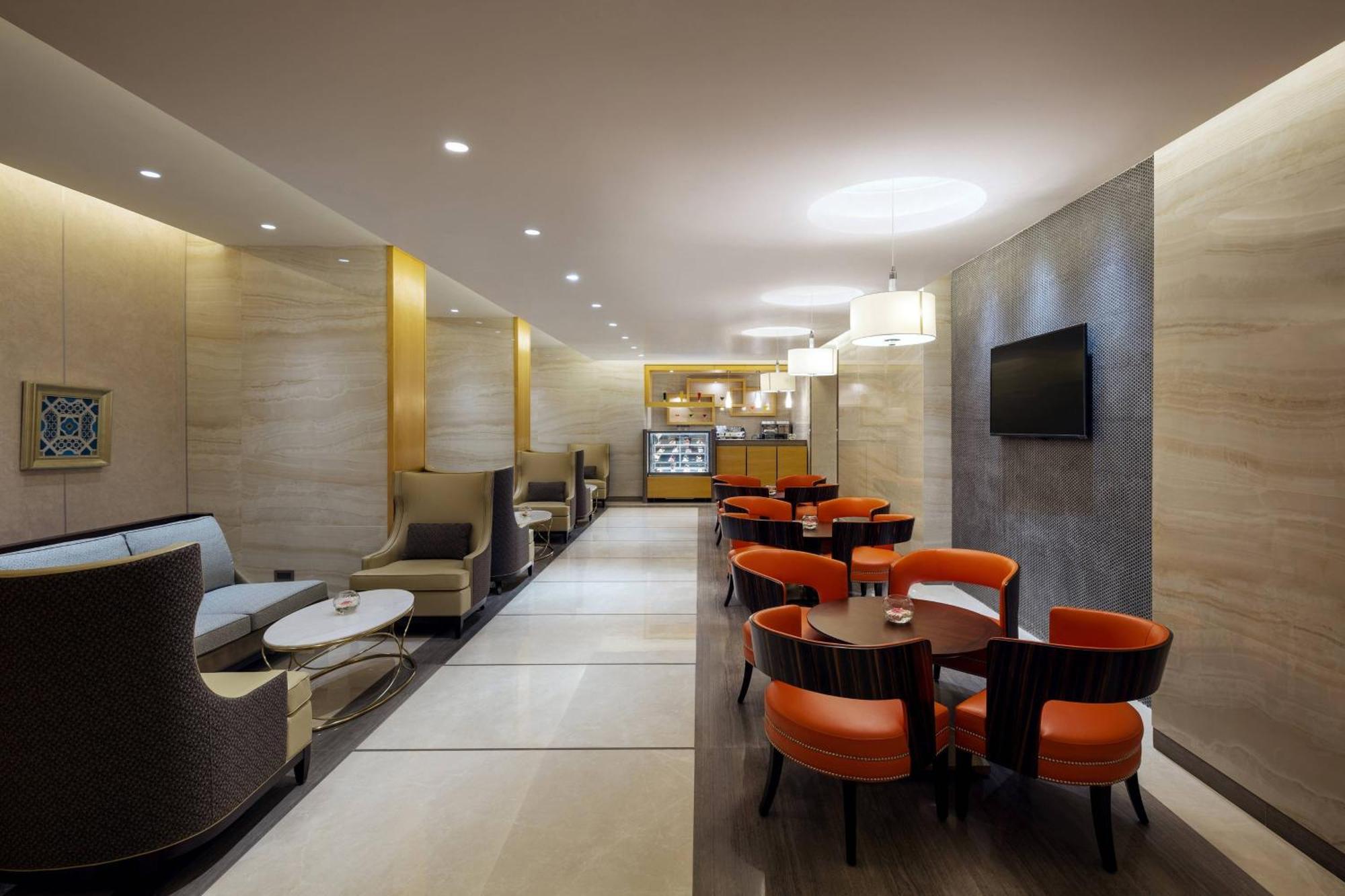 喜来登麦加贾巴尔卡巴酒店 Mecca 外观 照片 The photo depicts a modern and elegant lounge or café area. The interior features soft, warm lighting and a combination of neutral and bold color schemes. On the left side, there are comfortable seating arrangements with light-colored sofas and chair