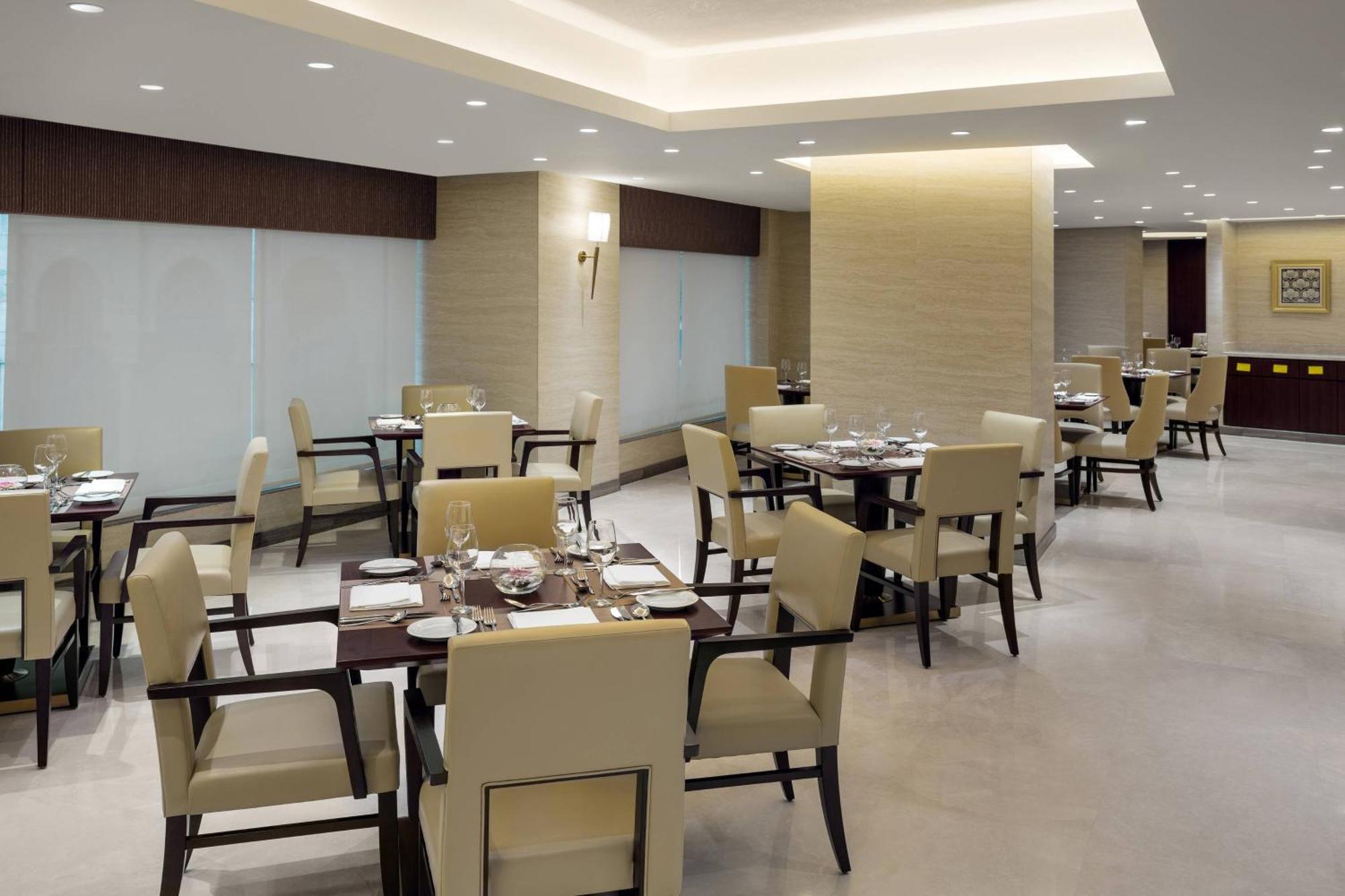 喜来登麦加贾巴尔卡巴酒店 Mecca 外观 照片 The photo shows a modern restaurant interior. It features several dining tables, each set with utensils and tableware. The chairs are upholstered in a light fabric, and the overall decor is sleek and minimalistic, with soft lighting from overhead fix