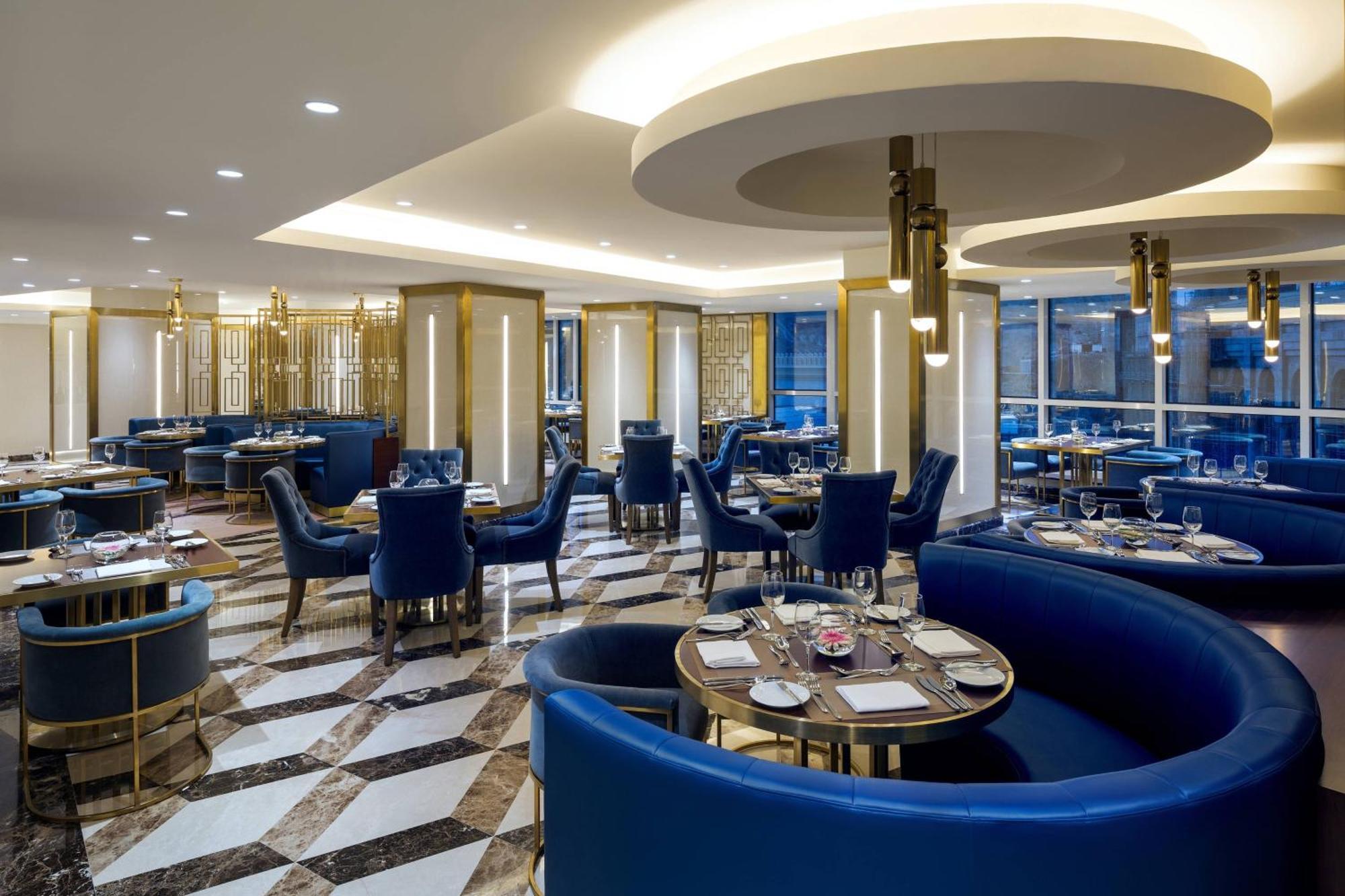 喜来登麦加贾巴尔卡巴酒店 Mecca 外观 照片 The photo shows the interior of a modern restaurant. The design features elegant curved blue seating arranged around round tables with plates and glassware set for dining. The flooring is a striking marble pattern, adding to the upscale ambiance. The